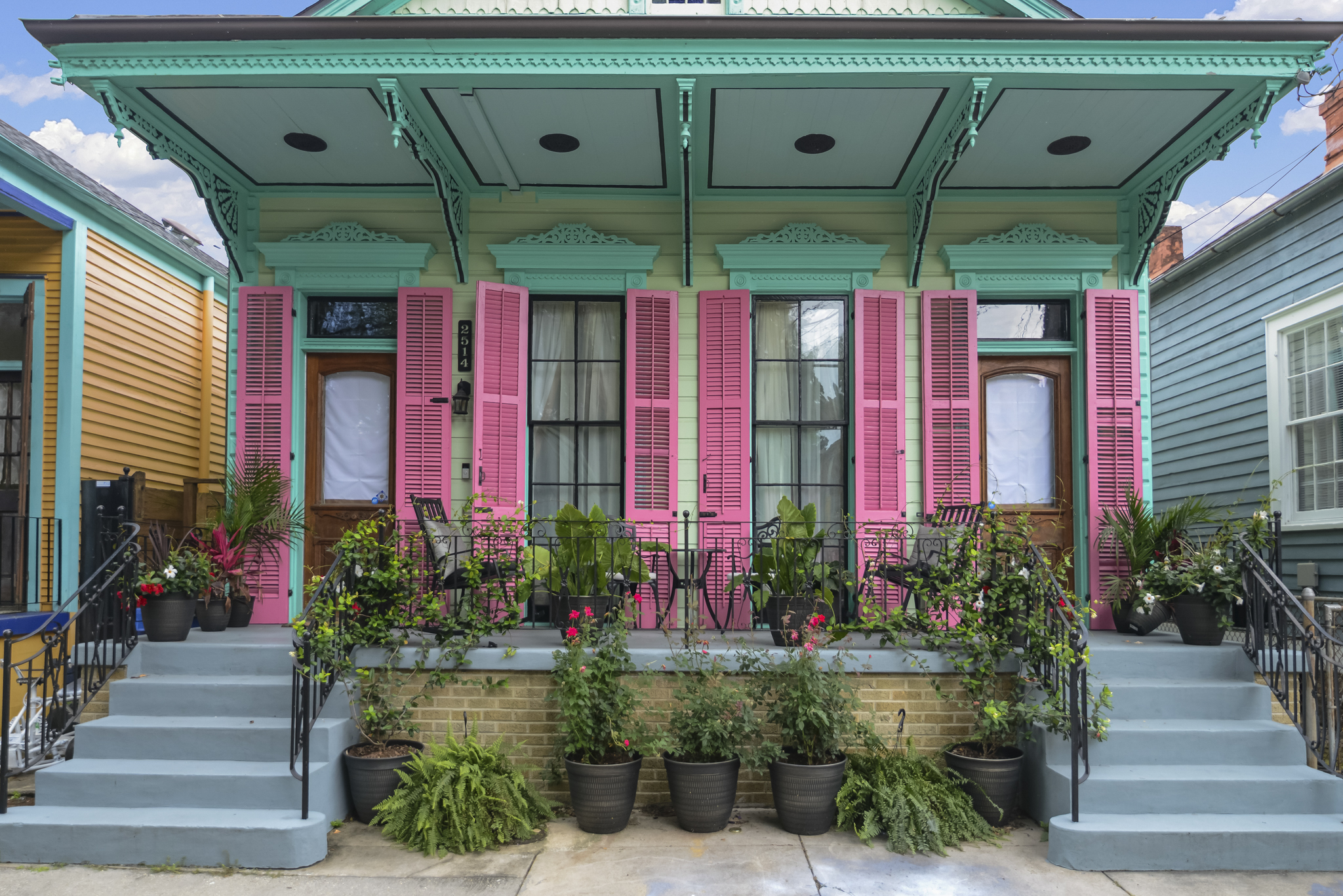 A colorful New Orleans Creole cottage with gingerbread trim, pink shutters and a planted front porch